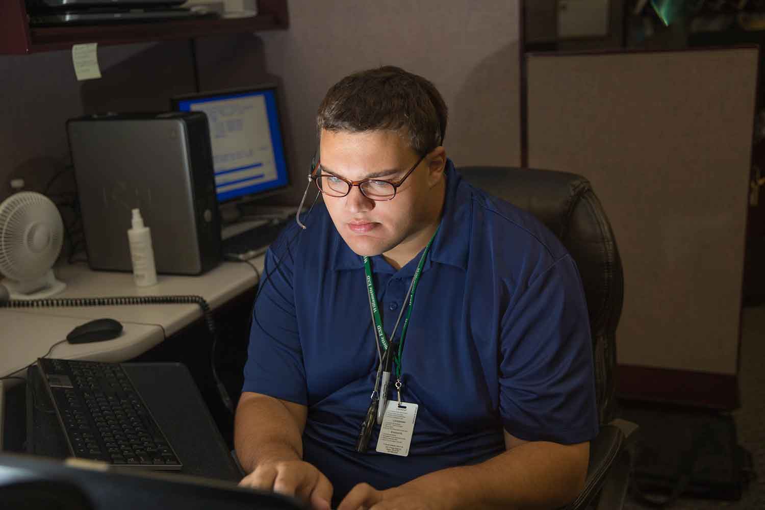 A student works at a computer while wearing a phone headset